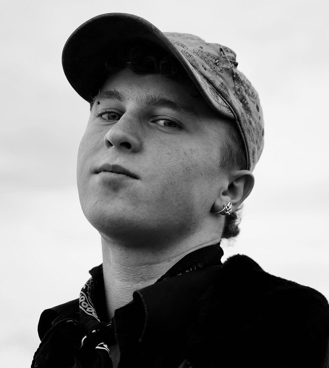 Black and white portrait of a young man in a cap against a bright sky