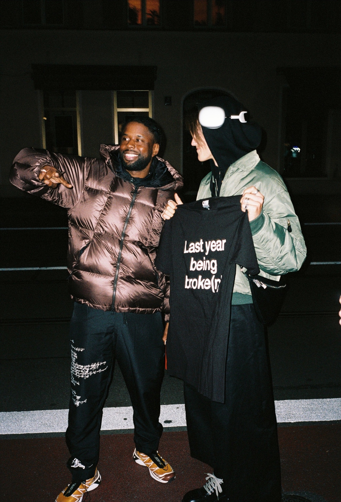 Two people at night holding up a printed black t-shirt on the street