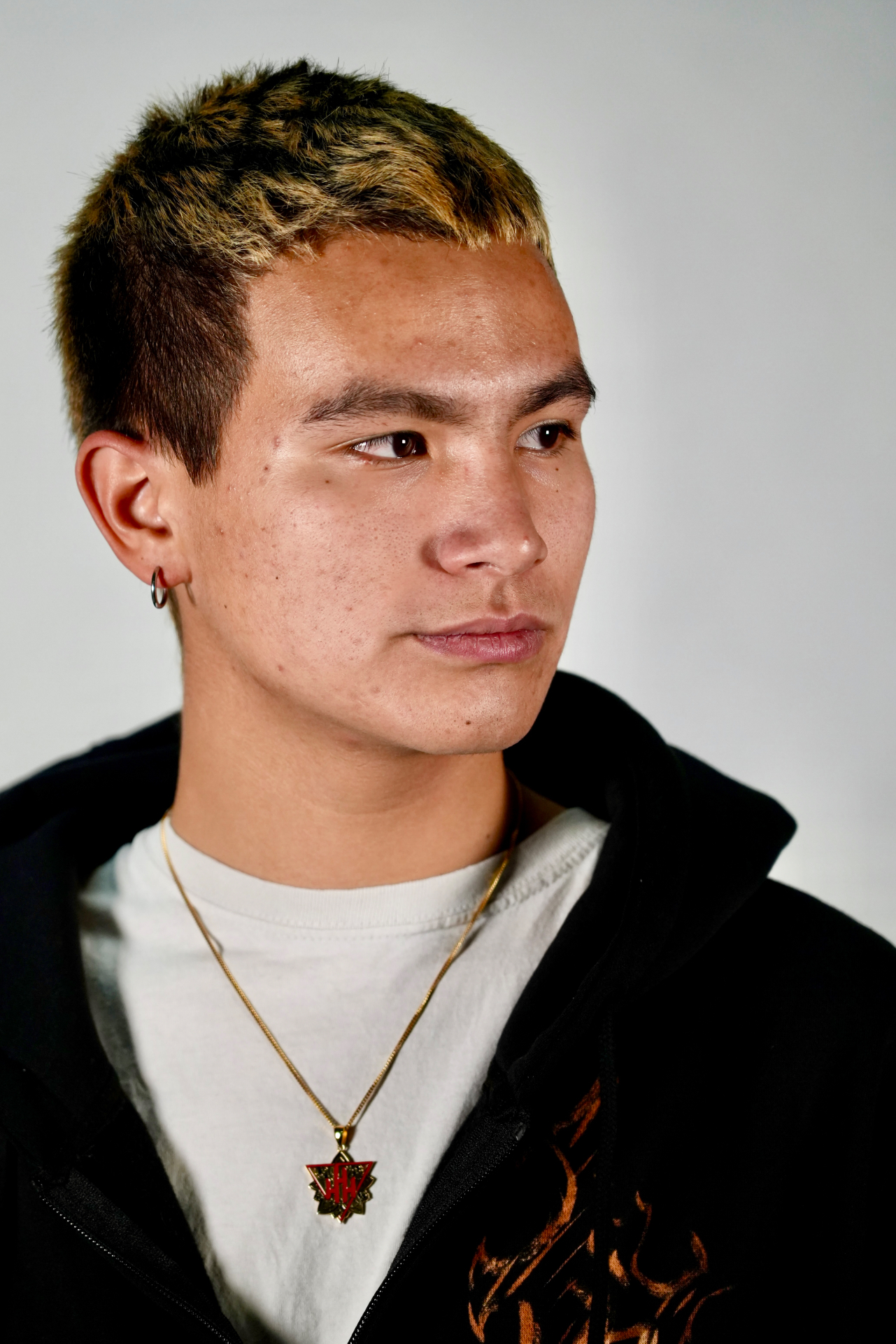 Close-up portrait of a young man with bleached hair and a gold pendant necklace