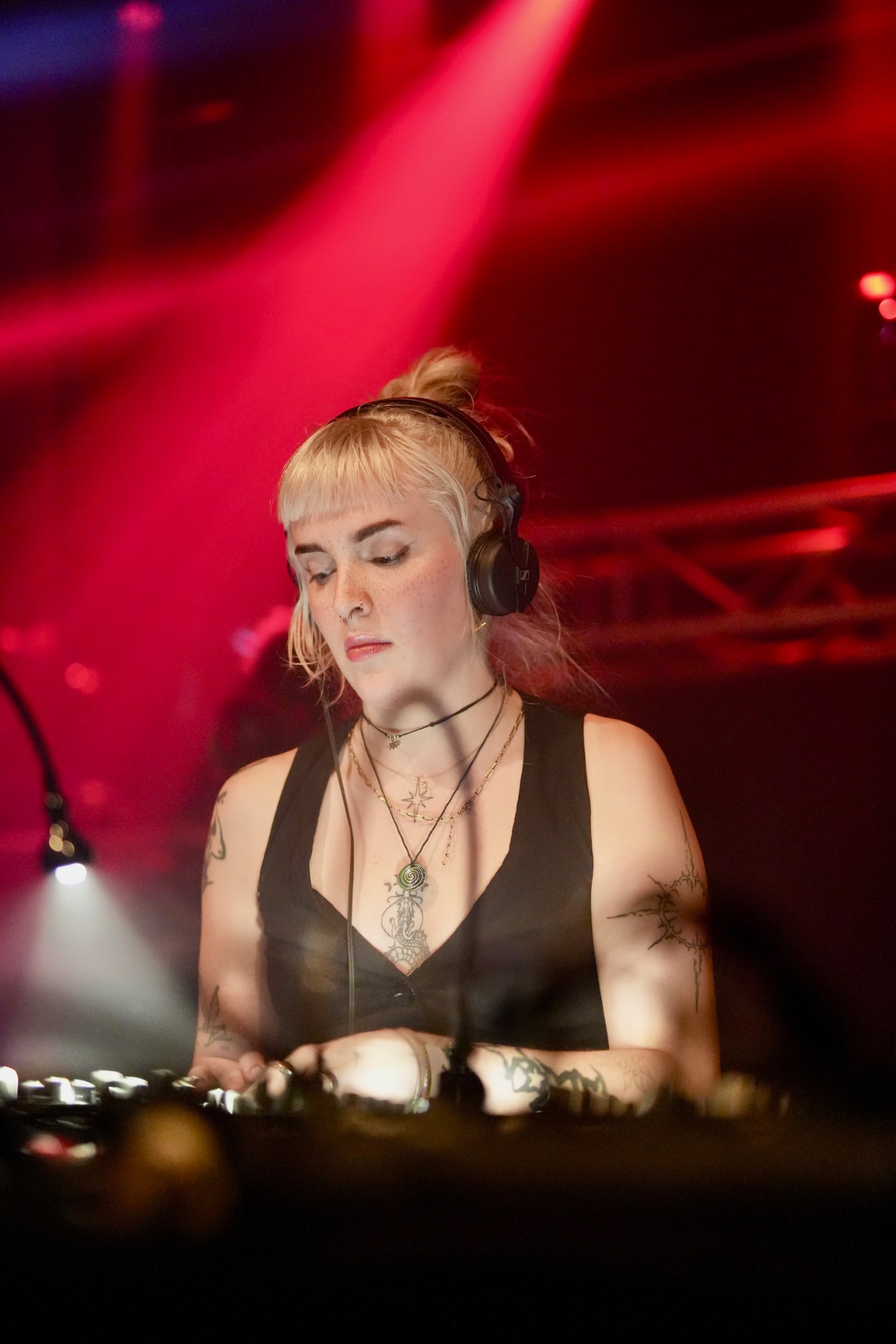 A DJ in headphones lit by red stage light behind a mixing desk