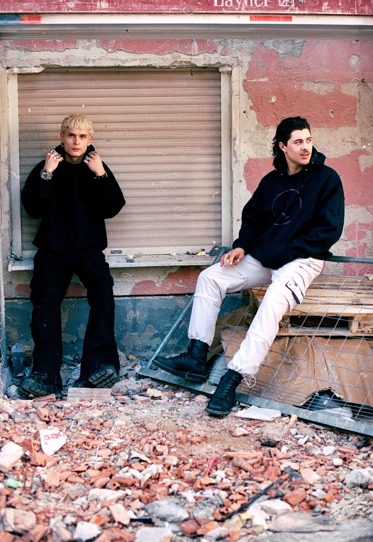 Two men in dark clothing at a demolished shopfront surrounded by broken brick