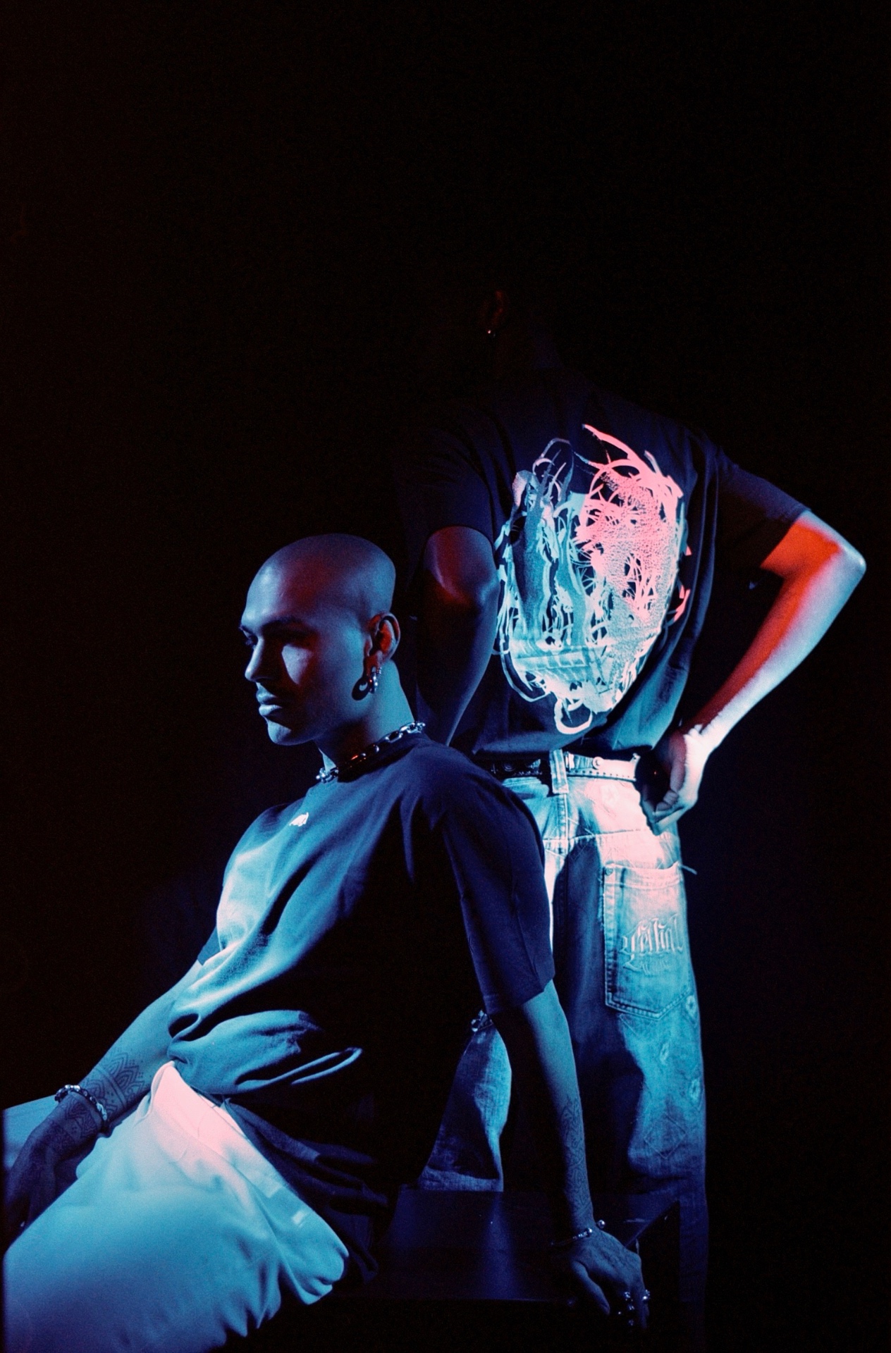 Two figures lit by blue and red light against a black background