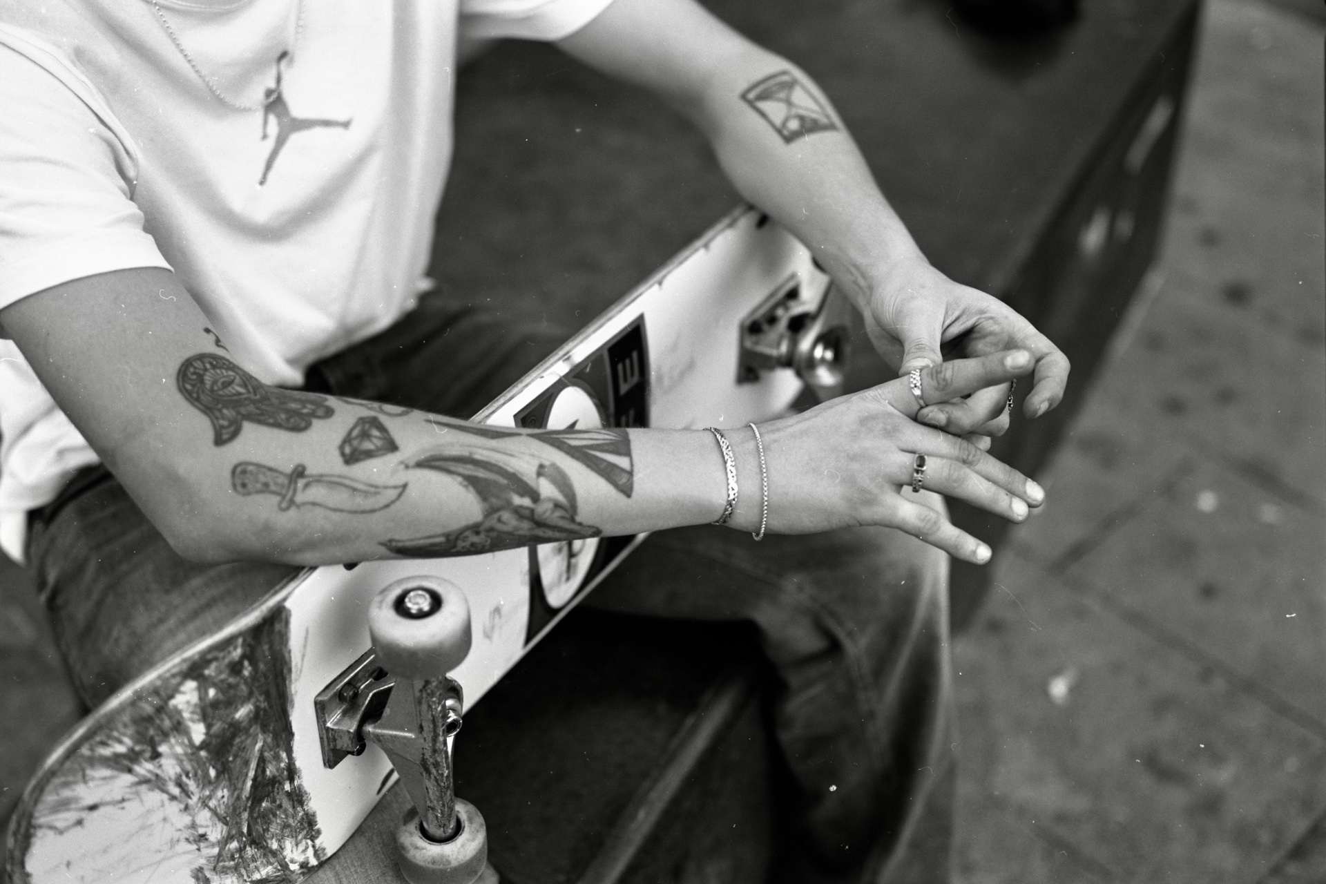 Black and white film photograph of tattooed hands resting on a skateboard